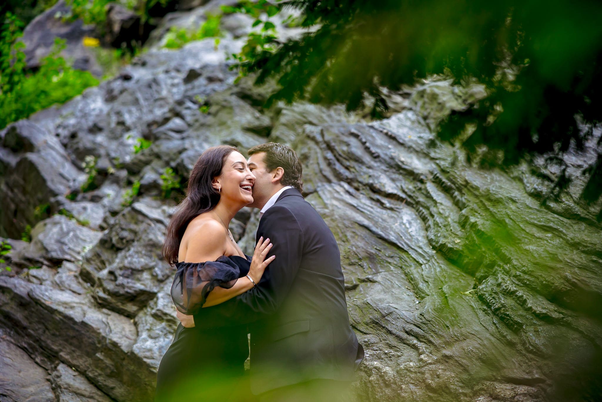 Engaged couple laughing together in front of a rocky cliff during a romantic outdoor photo session