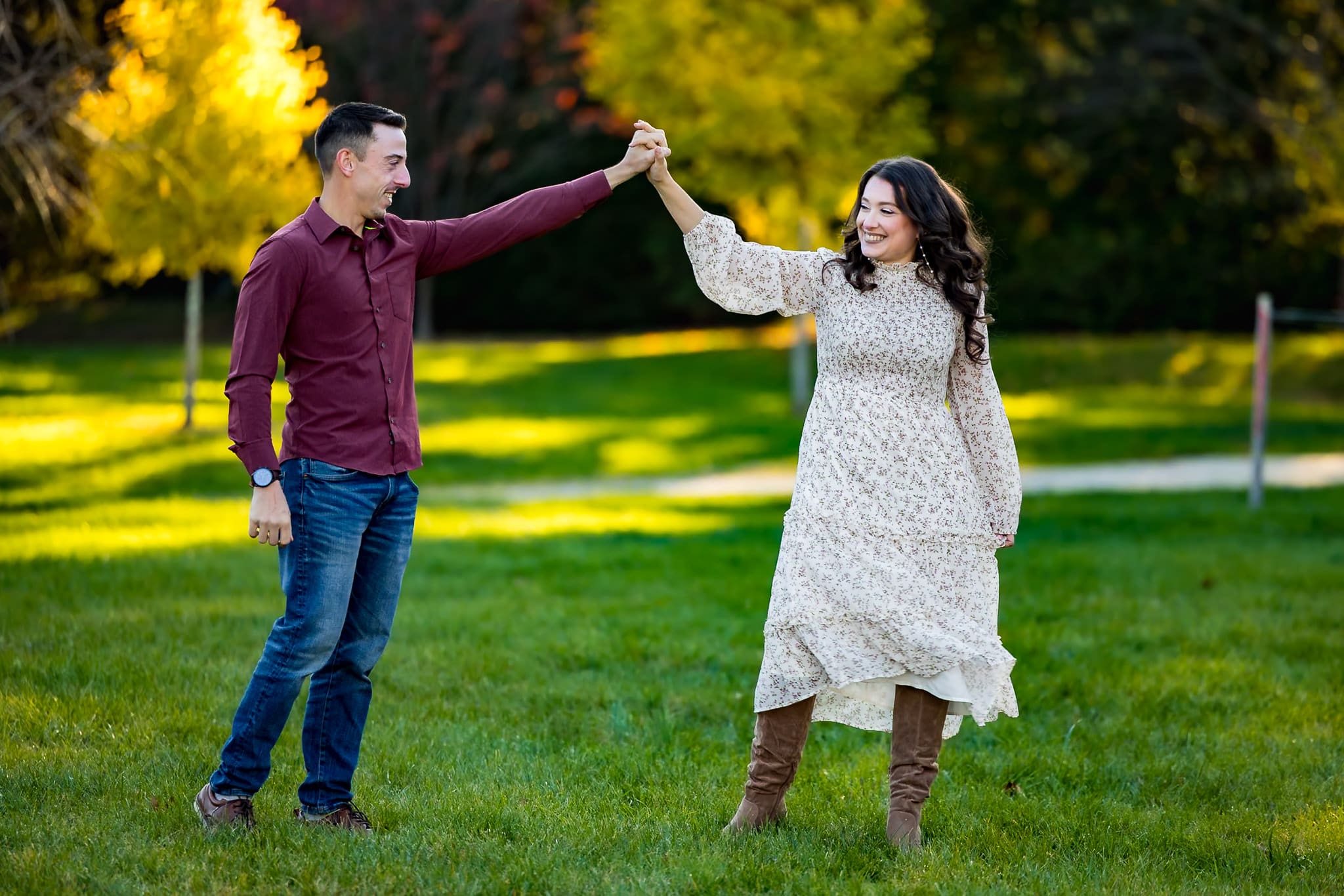 Couple dancing together in a sunlit park during their fall engagement photo session.