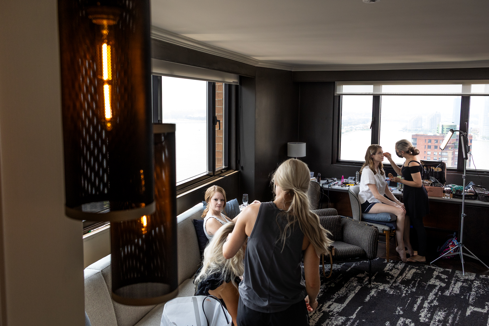 Two women get their hair styled by professionals in a well-lit modern room, preparing for the day as hairstyling tools fill the space. Such moments are often captured while exploring New Jersey wedding photography costs.
