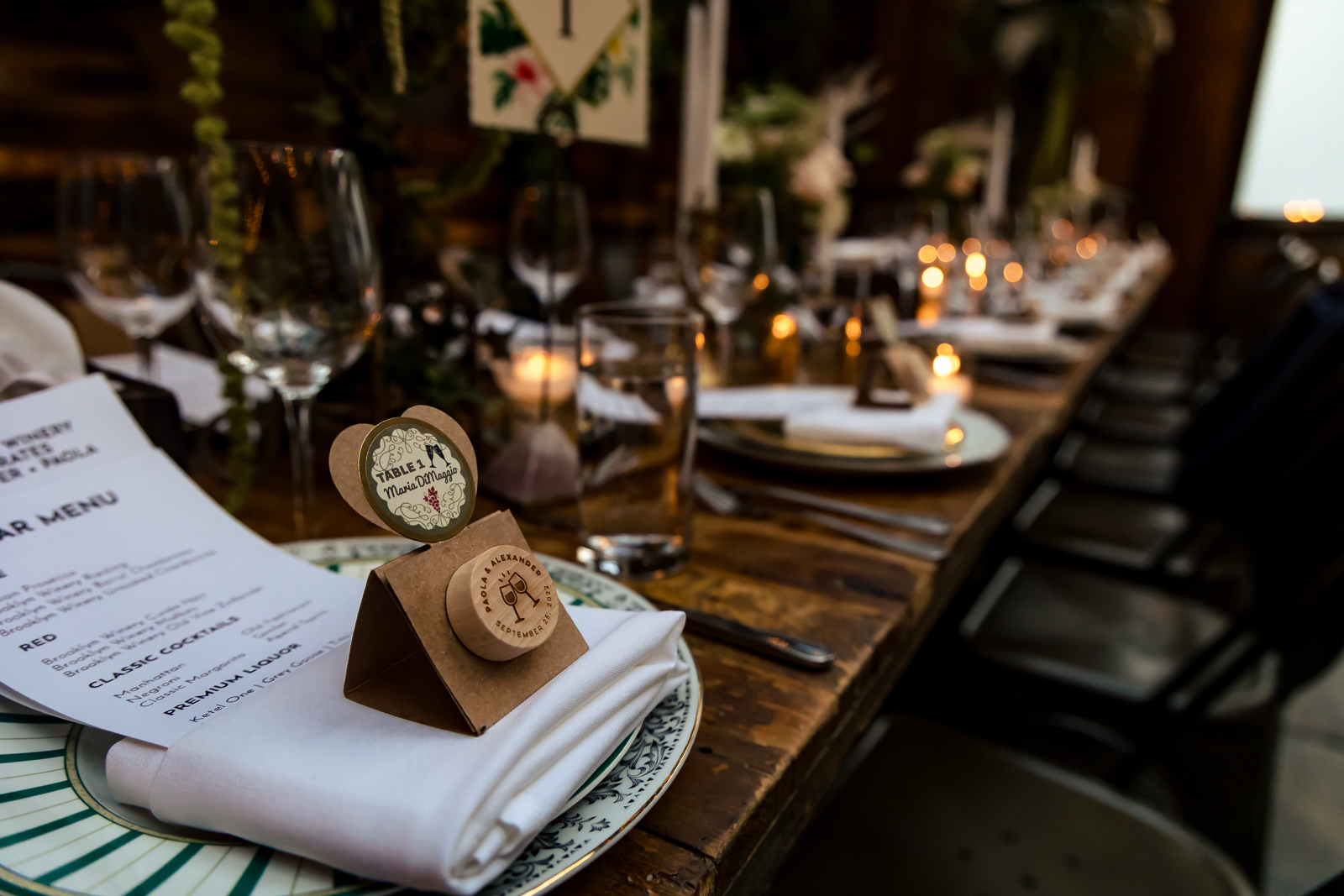 A decorated dinner table set for an event with menus, candles, wine glasses, and small favor boxes on each plate, creating an elegant and inviting atmosphere.